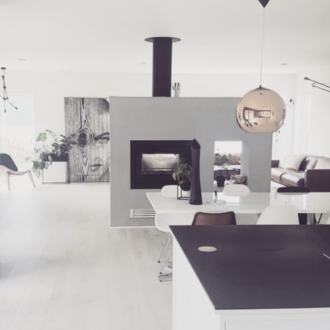 Sort peisinnsats Scan DSA 12 med innsyn fra to sider bygget inn i en plassbygget lys grå peis med vednisje  midt i rommet i en hvit stue