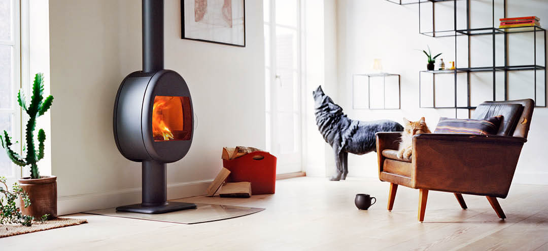 Sort vedovn på søyle Scan 66-2 i moderne hvit stue med rød vedkurv, skinnstol med en rød katt.