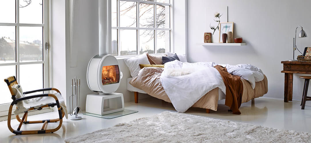 Hvit vedovn Scan 66-4 med eggeformet brennkammer på rektangulær base i et hvitt soverom med store vinduer