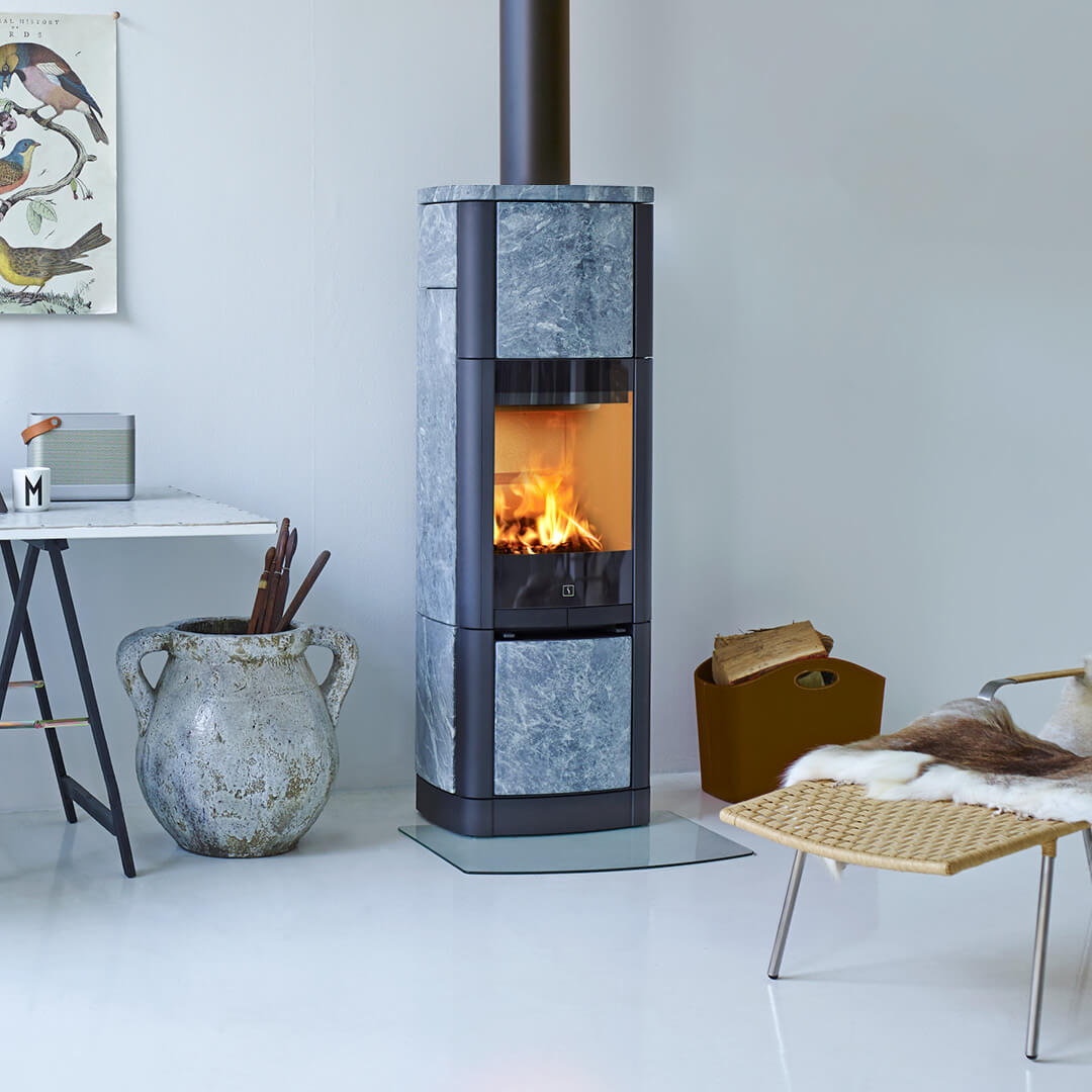 Høy vedovn kledd med kleberstein Scan 65 High Top i en hvit stue med et skrivebord og en stol i rotting