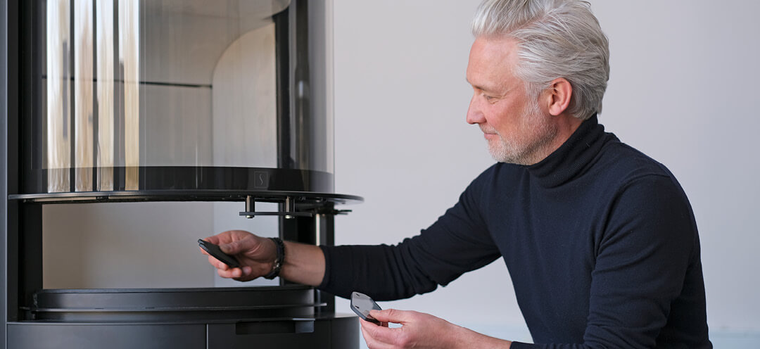 Middelaldrende mann i høyhalset genser designer Niels Kjeldsen viser glasshåntak foran peis Scan 87