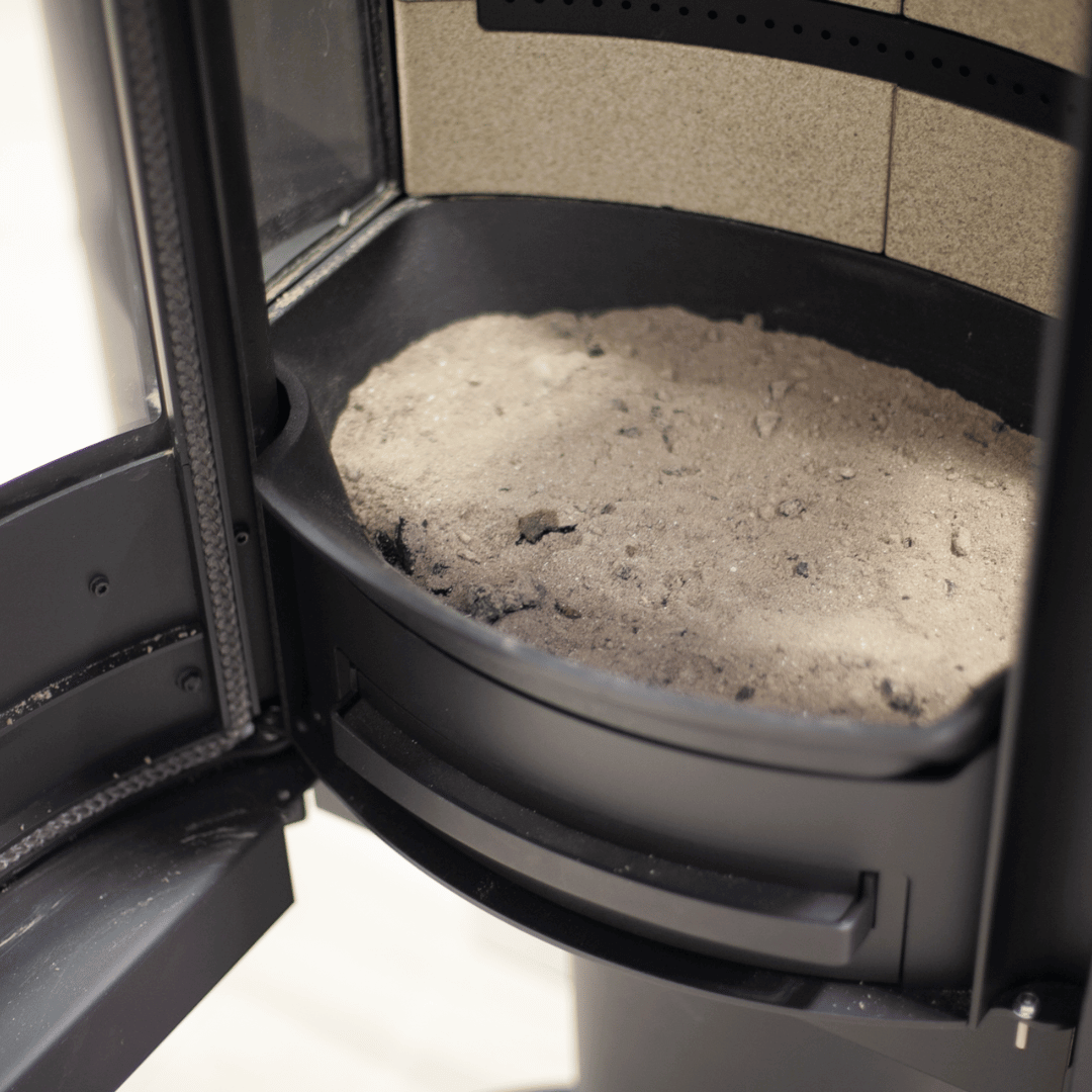 Aske i fyrbunnen på vedovn, klar for tømming eller bruk til rengjøring av peisglass