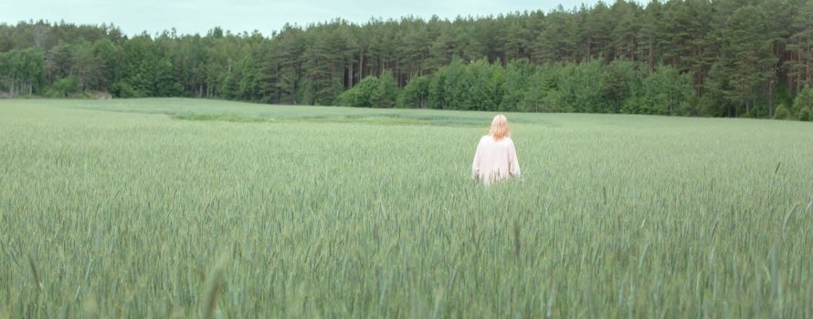 Dame I hvit kjole som går i en åker