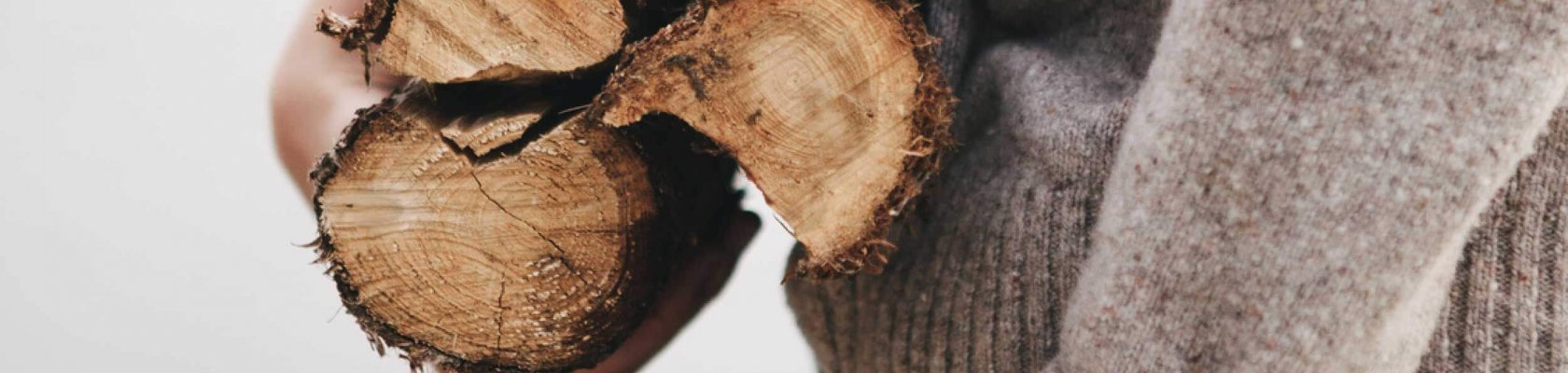 Gutt med beige stikkegenser som holder 3 vedkubber under armen