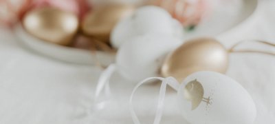 Påskepynt egg i rosa, hvitt og gull som ligger på et hvitt bord