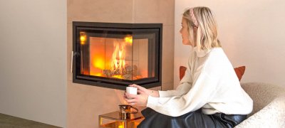 Blond kvinne sitter foran en peis med en kopp i hendene