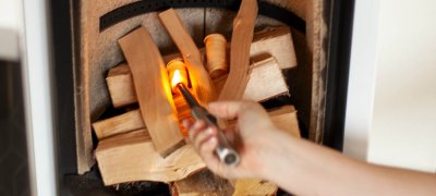 Hånd som tenner på peisen i en hvit vedovn Scan 83-2 