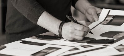 Sort hvitt bilde av hendene til en mann står ved et bord og tegner på skisser av Scan 87 vedovn