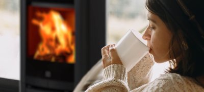 Jente med mørkt hår og hvit ullgenser drikker av hvit kopp foran vedovn Scan 65-1