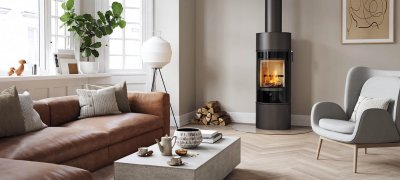 Sort rund vedovn Scan 84 med sort glassdør I en moderne nordisk stue med brun sofa og lysegrå stol