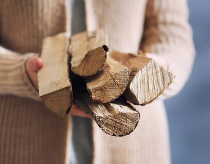 Kvinne i beige strikkejakke som bærer ved i hendene