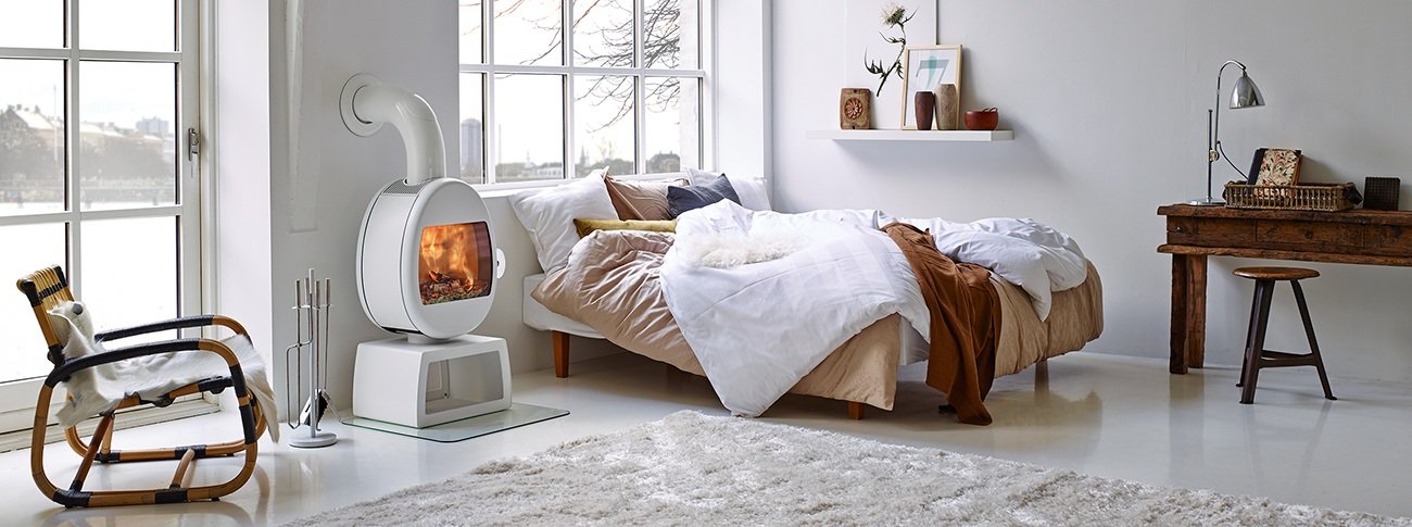 Hvit vedovn Scan 66-4 ved siden av seng i hvitt soverom og skrivebord i mørkt tre