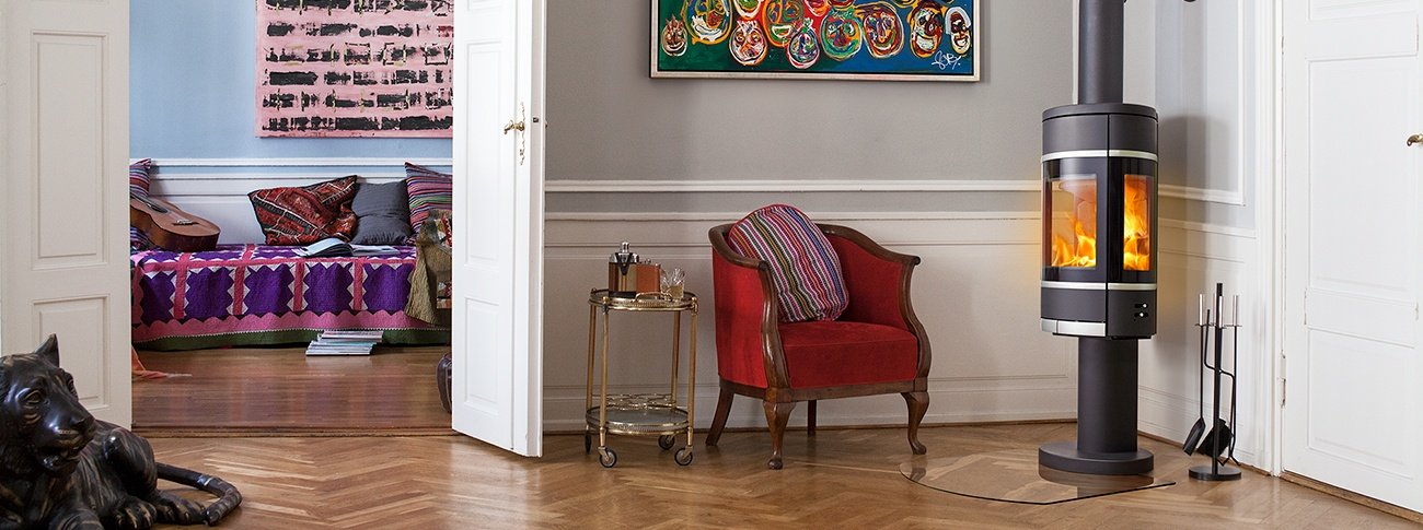 Svart vedovn Scan 68-10 på søyle med glass på flere sider, aluminiumsdekor og oval form i klassisk stue med eksotiske interiørdetaljer