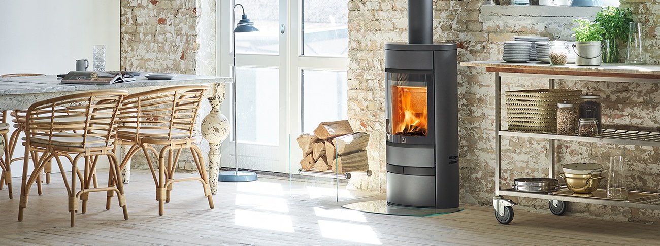 Liten vedovn Scan 68-13 Low Base med stor glassdør og eksklusive sorte glassdetaljer i kjøkkeninteriør med lys sandfarget mur, bambus spisestue og verandadør