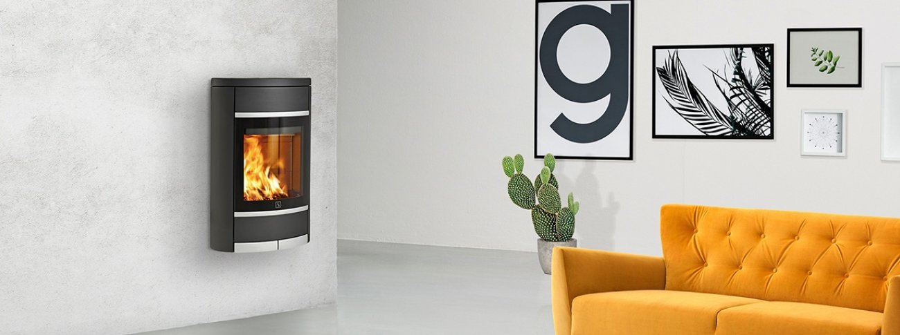 Vegghengt vedovn Scan 68-2 sort med stor glassdør og aluminiumsdetaljer i mockup industrielt interiør med gul sofa