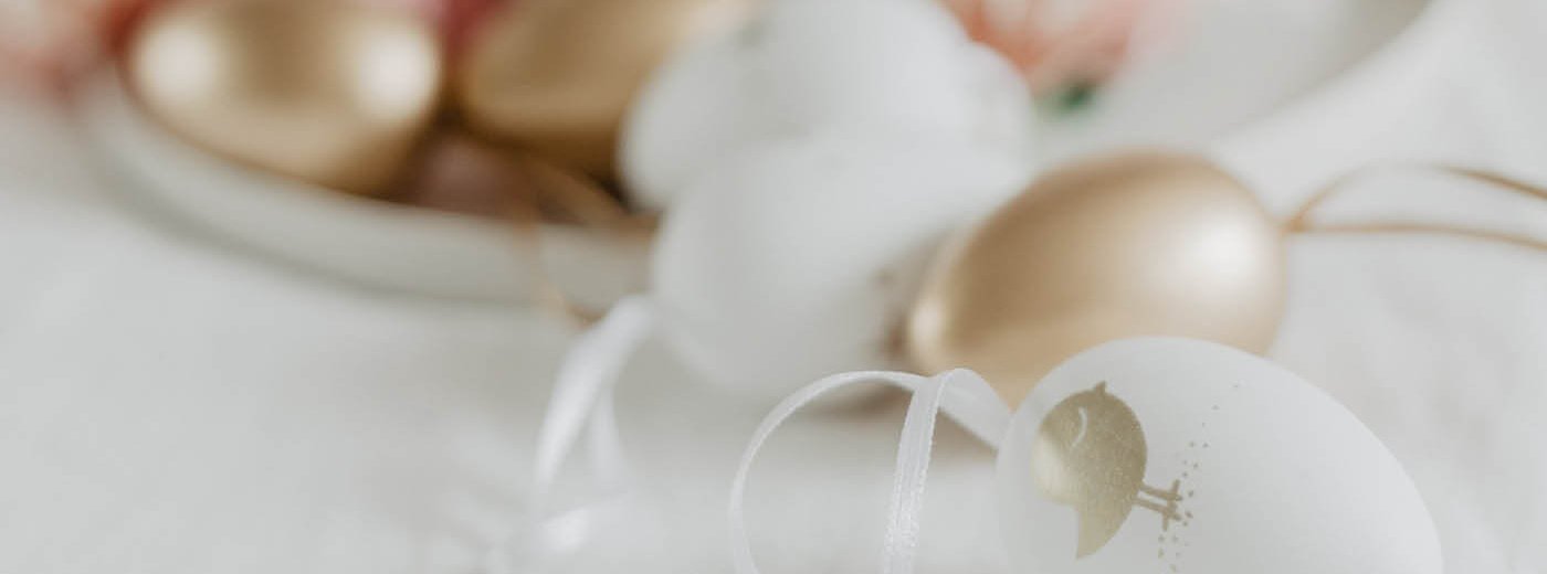 Påskepynt egg i rosa, hvitt og gull som ligger på et hvitt bord