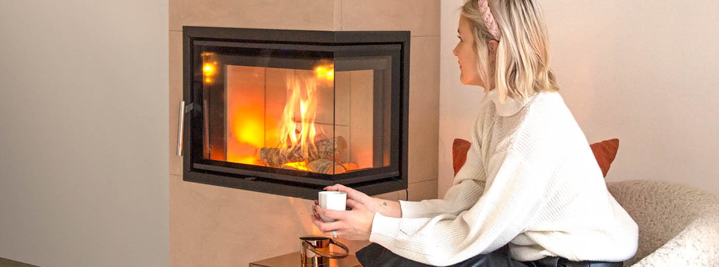 Blond kvinne sitter foran en peis med en kopp i hendene