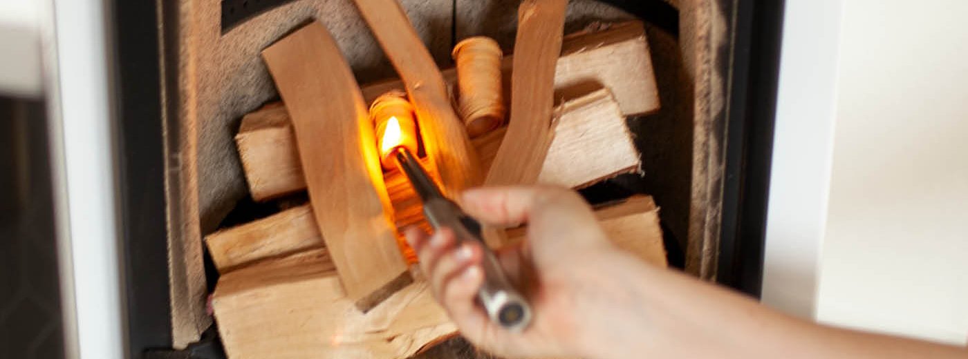 Hånd som tenner på peisen i en hvit vedovn Scan 83-2 