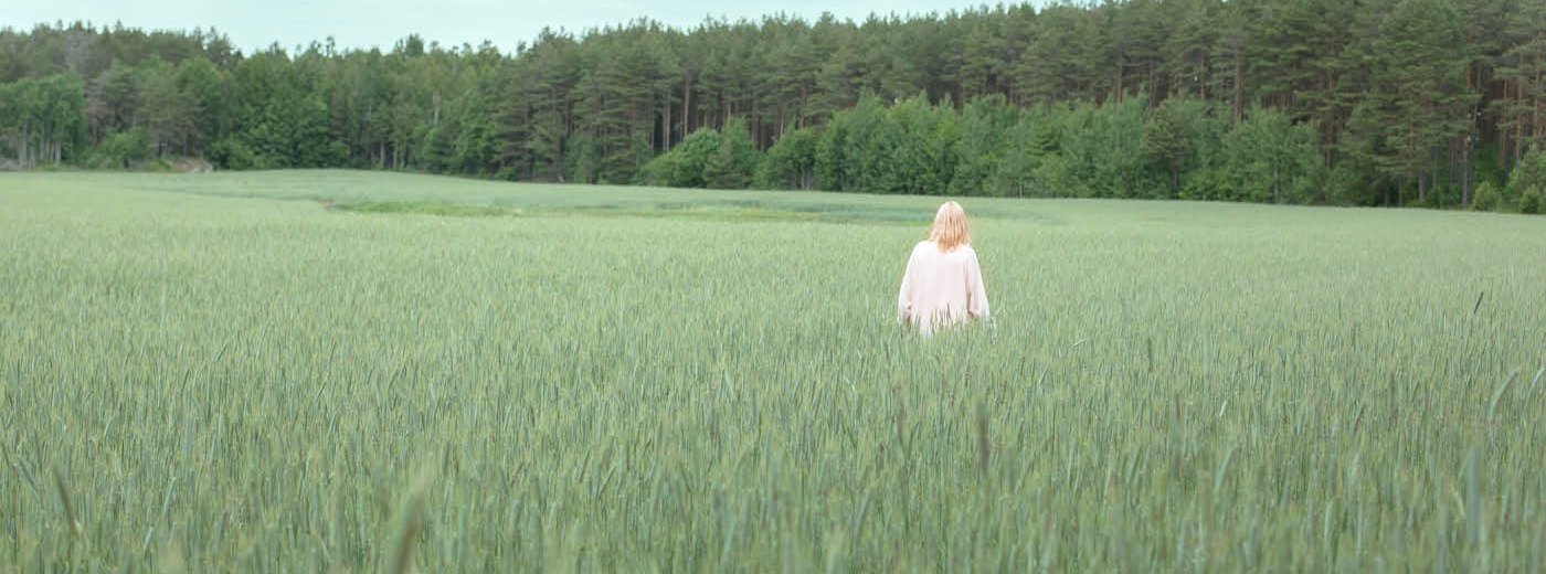 Dame I hvit kjole som går i en åker