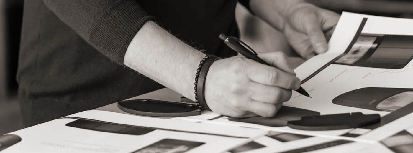 Sort hvitt bilde av hendene til en mann står ved et bord og tegner på skisser av Scan 87 vedovn