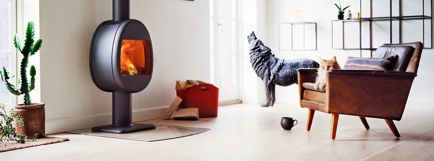 Liten vedovn eggeformet på søyle Scan 66-2 svart farge i stue med skinnstol med katt og statue av ulv 