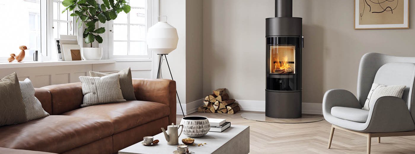 Sort rund vedovn Scan 84 med sort glassdør I en moderne nordisk stue med brun sofa og lysegrå stol