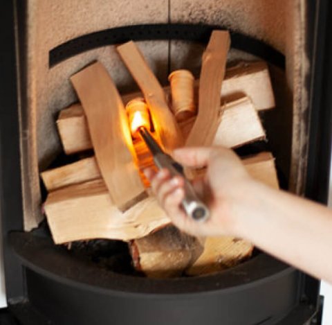 Hånd med lighter som tenner på et bål i peisen