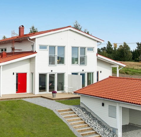 Hvitt hus tomannsbolig med orange tak og carport 