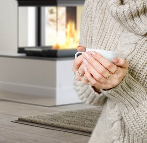 Detaljbilde av kvinne med beige genser som holder en hvit kopp i hendene, i bakgrunnen kan man se en avlang peisinnsats Scan 5005 FRL