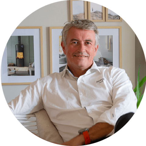 En mann i en hvit skjorte, René Christensen, Senior Vice President Sales & Marketing, sitter i en stol foran en vegg med bilder av Scan vedovner