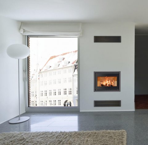 Sort peisinnsats med flammer Scan 1005  innfelt i veggen i en hvit stue med store vinduer